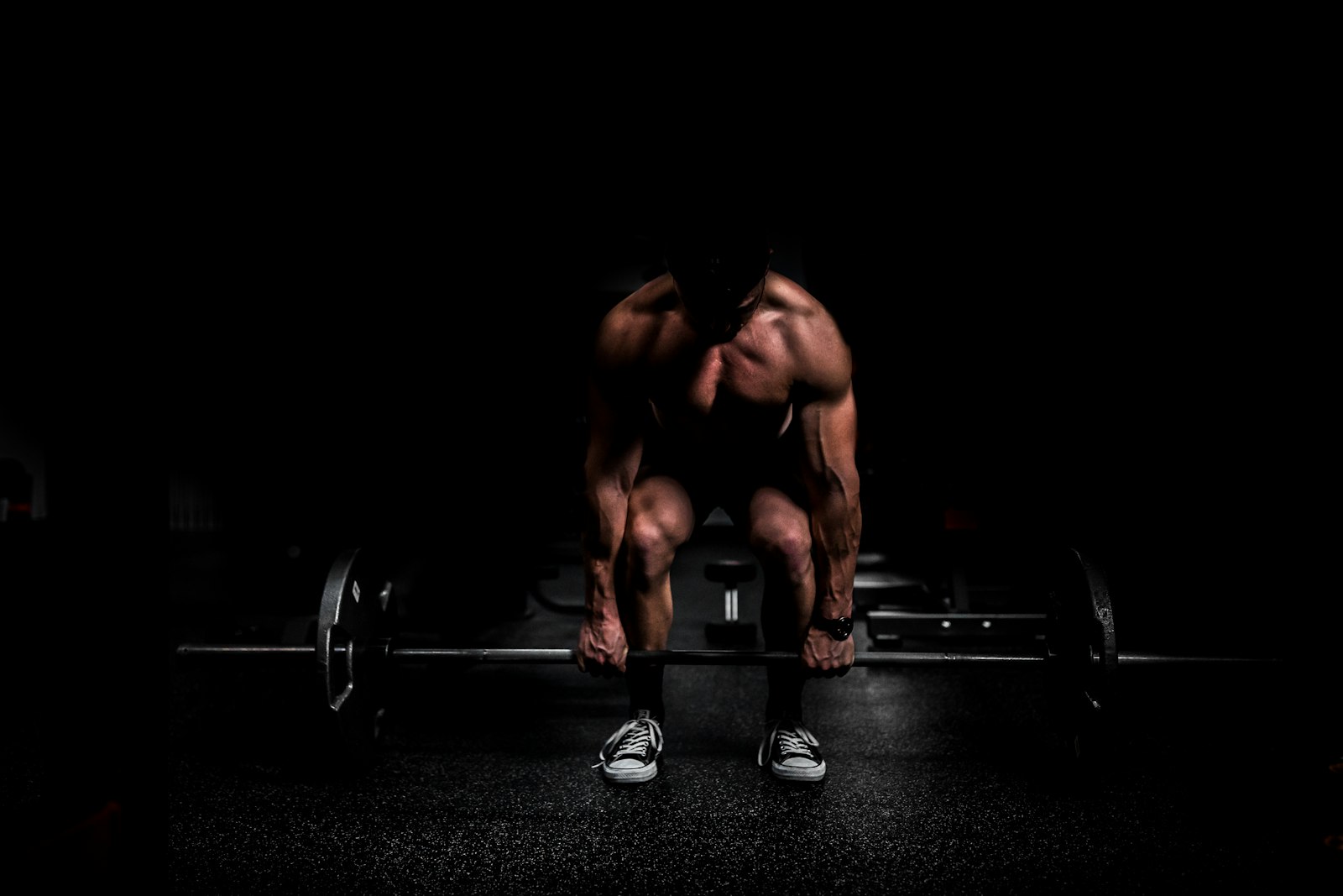 Muscular athlete deadlifting a barbell in a dark gym